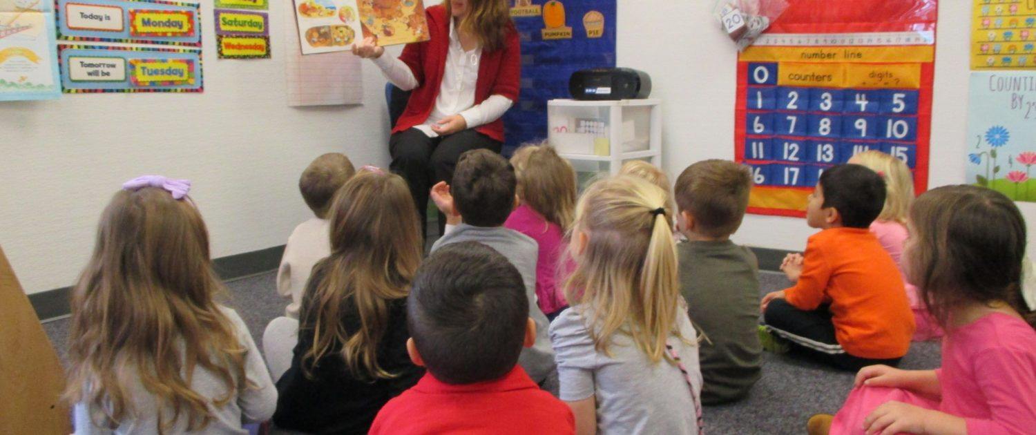 children sitting and listening to their preschool teacher as she reads them a story.