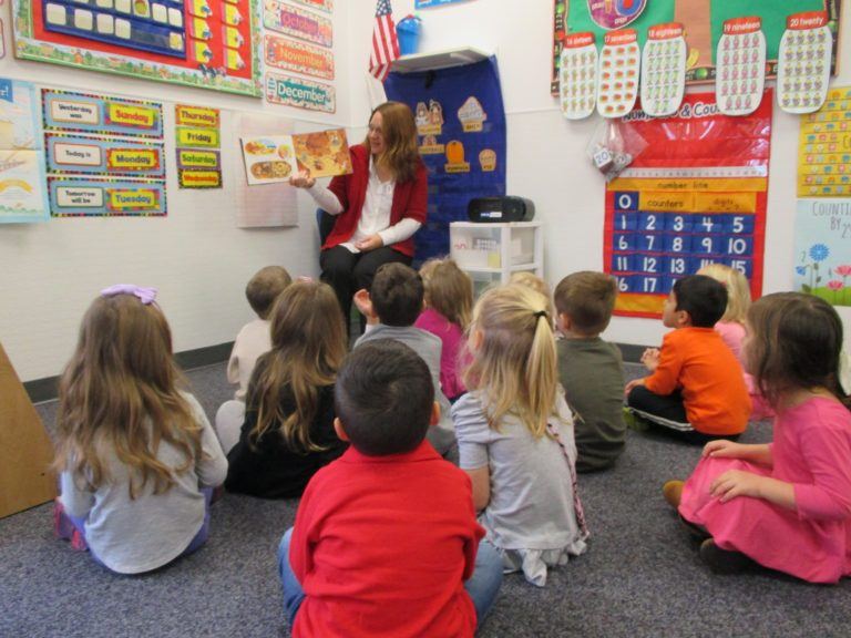 children sitting and listening to their preschool teacher as she reads them a story.