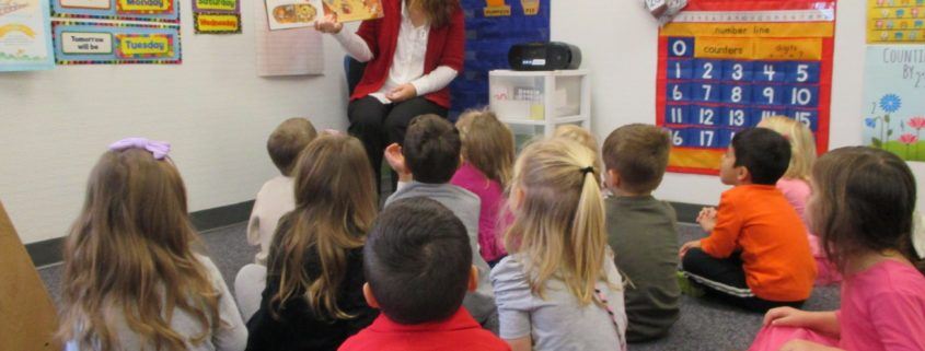 children sitting and listening to their preschool teacher as she reads them a story.