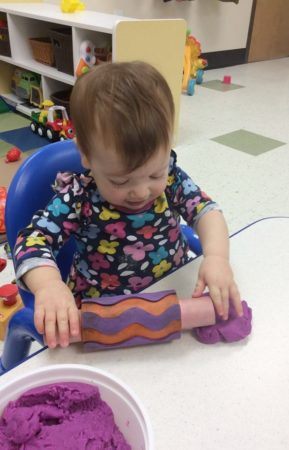 2-year-old_using_a_rolling_pin_on_playdough_creative_expressions_learning_center_imperial_mo-289x450