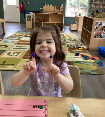 Little girl holding up pointer fingers covered in paint while doing a hands-on activity at DuPont preschool and daycare Cadence Academy Preschool Washington