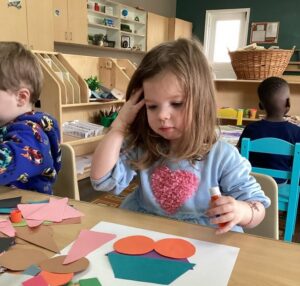 young girl using cutout shapes of construction paper to make craft at cadence academy preschool and daycare in dupont washington