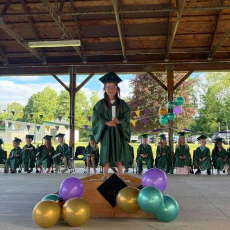 Child standing on stage with classmates behind her at graduation at Creative Kids Childcare Centers Beekman