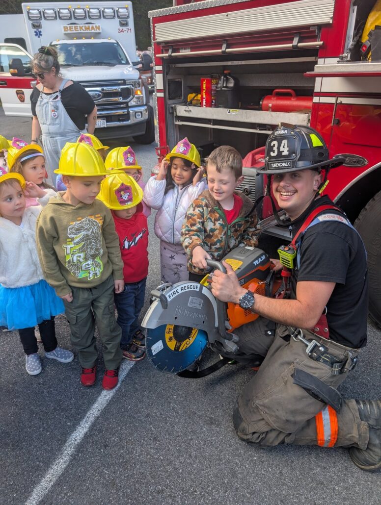 Children gathered around firetruck with firefighter learning at Creative Kids Childcare Centers Beekman
