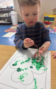 Child painting hand green to create art at Creative Kids Childcare Centers Beekman