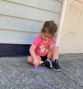 young girl squatting on floor to draw outside with chalk at cadence academy preschool and daycare in dupont washington