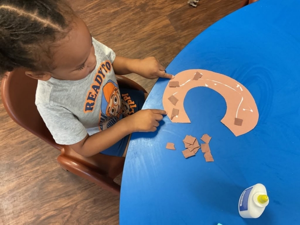 Child gluing paper at desk at Cadence Academy Preschool Olive Branch, Mississippi