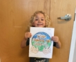 Child holding up colored in picture of world smiling at Cadence academy preschool and daycare 505 murfreesboro