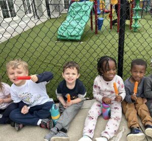 Children sitting outside by playground against a fence eating popsicles and smiling at Cadence academy preschool and daycare 505 murfreesboro