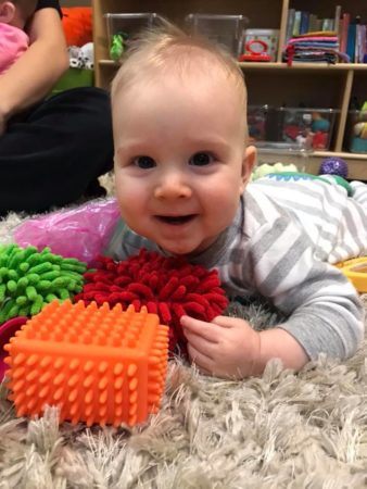 happy_toddler_playing_with_toys_on_soft_carpet_cadence_academy_preschool_sellwood_portland_or-338x450