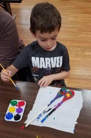 preschool_boy_painting_spoons_miss_muffets_learning_center_klamath_falls_or-297x450