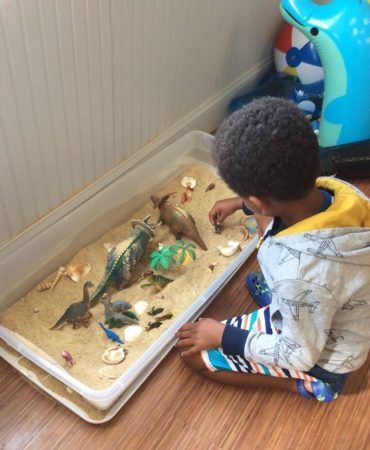 preschool_boy_playing_in_sand_with_dinosaurs_winwood_childrens_center_ashburn_va-370x450