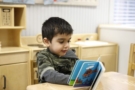 preschool_boy_reading_book_at_table_winwood_childrens_center_leesburg_va-675x450