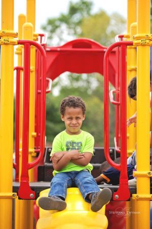 preschool_boy_sitting_on_playground_cadence_academy_preschool_rosemeade_carrollton_tx-300x450