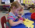 preschool_girl_cutting_paper_with_scissors_cadence_academy_preschool_centennial_co-562x450