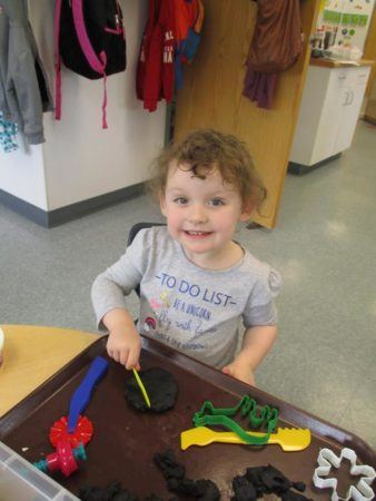 preschool_girl_cutting_shapes_into_playdough_adventures_in_learning_oswego_il-338x450