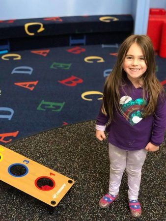 preschool_girl_enjoying_bean_bag_toss_game_cadence_academy_preschool_hanover_ma-338x450