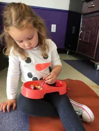 preschool_girl_picking_up_fuzzy_balls_with_tweezers_canterbury_academy_at_shawnee_crossings_shawnee_ks-338x450