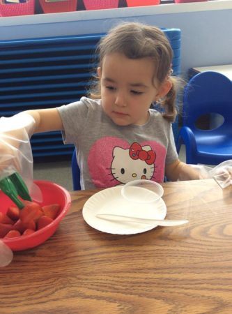 preschool_girl_picking_up_strawberry_with_tongs_at_next_generation_childrens_centers_westborough_ma-333x450