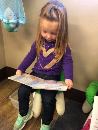 preschool_girl_reading_a_book_on_a_stool_at_cadence_academy_preschool_broomfield_co-338x450