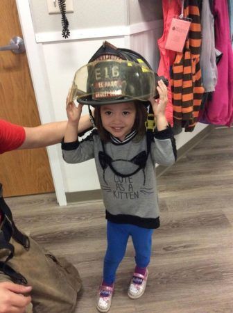 preschool_girl_trying_on_firefighter_helmet_cadence_academy_preschool_main_street_normal_il-336x450