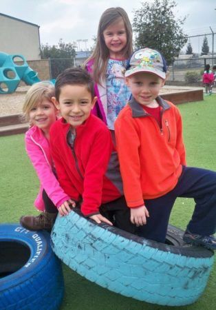 preschoolers_posing_in_tire_on_playground_at_cadence_academy_preschool_broadstone_folsom_ca-314x450