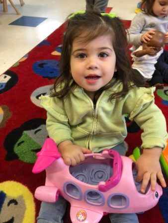 toddler_girl_holding_a_pink_airplane_prime_time_early_learning_centers_farmingdale_ny-338x450