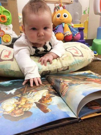 toddler_on_lounge_cushion_with_book_cadence_academy_preschool_iowa_city_ia-336x450