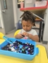 child playing in sensory bucket with pom poms