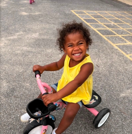 little girl smiling up while on a bike with training wheels