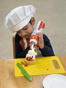 child decorating strawberry tarte with whipped cream at cadence academy preschool 453 pond