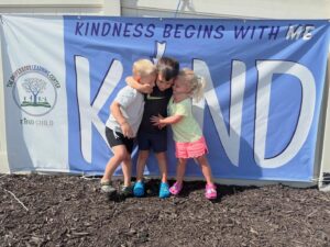 children smiling and hugging in front of kind child sign at the professors learning center daycare and preschool elkhorn NE 509