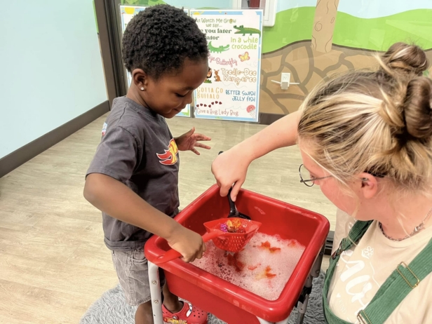 male child learning through hands on activity with teacher at watch me grow riggs
