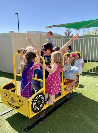 multiple children playing with teacher outside on playground equipment at watch me grow riggs