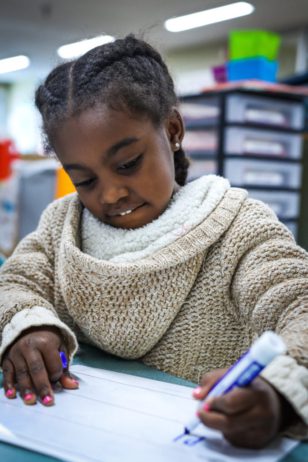 elementary girl in afterschool program practicing writing on a whiteboard in a classroom