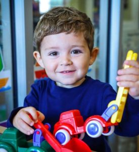 small boy in pre-k program plays with toys on a table and looking at the camera