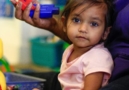 small girl sitting in lap of teacher looking at camera in her childcare program while the teacher shows her different toys