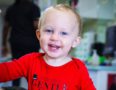 Toddler age boy smiling at camera with red shirt on in toddler care program