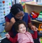 happy preschool teacher sitting with happy student in the reading and toy area of the classroom