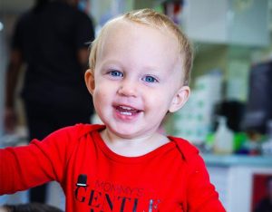 Toddler age boy smiling at camera with red shirt on in toddler care program